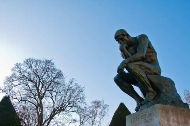 Statue of the thinker in front of trees and a blue sky