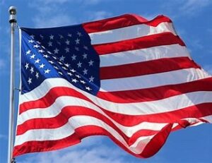 Large American flag attached to the top of a pole and flapping in the breeze. Blue sky background